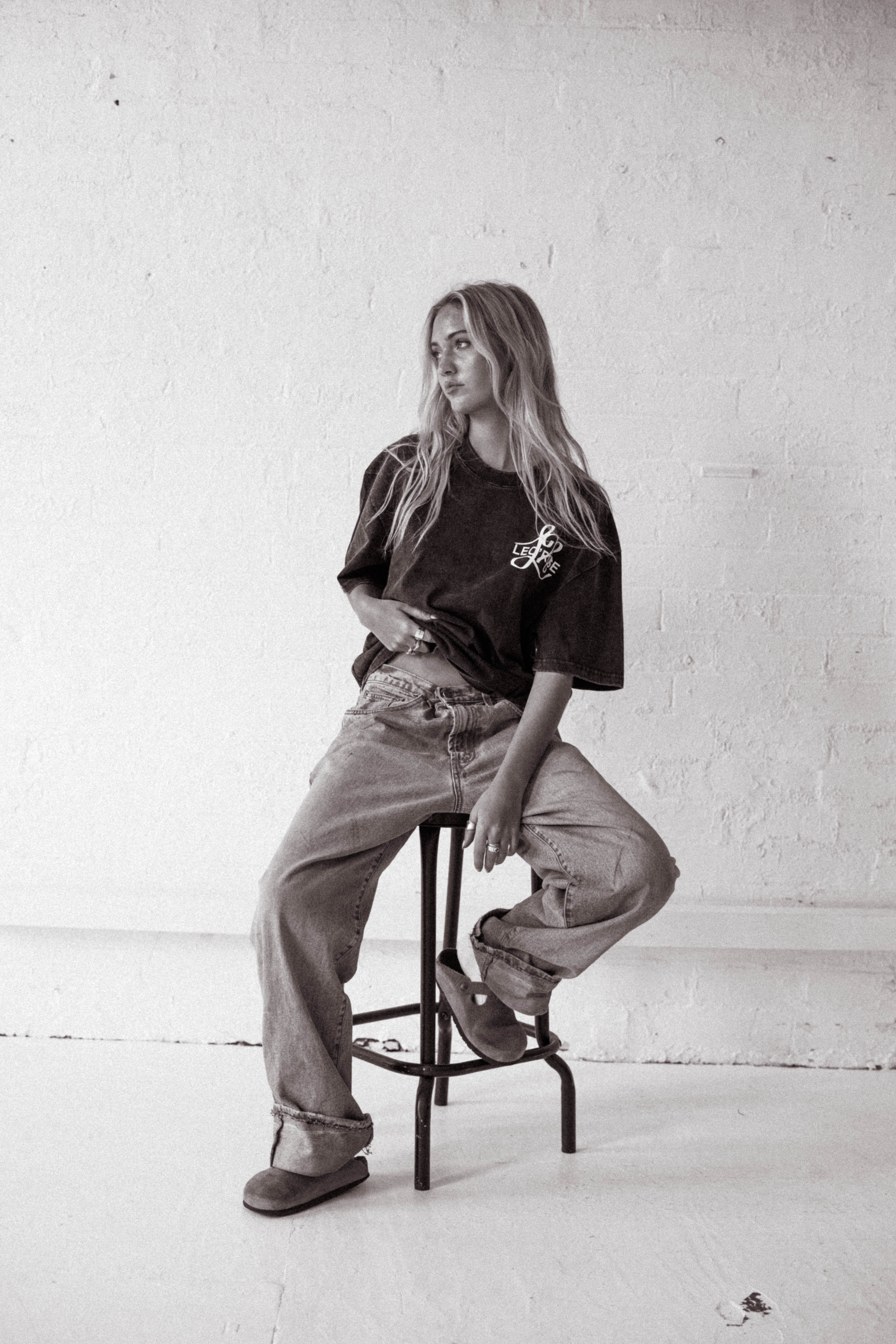 Female sitting on a stool looking away to the left from camera wearing LEO'ROSE tee