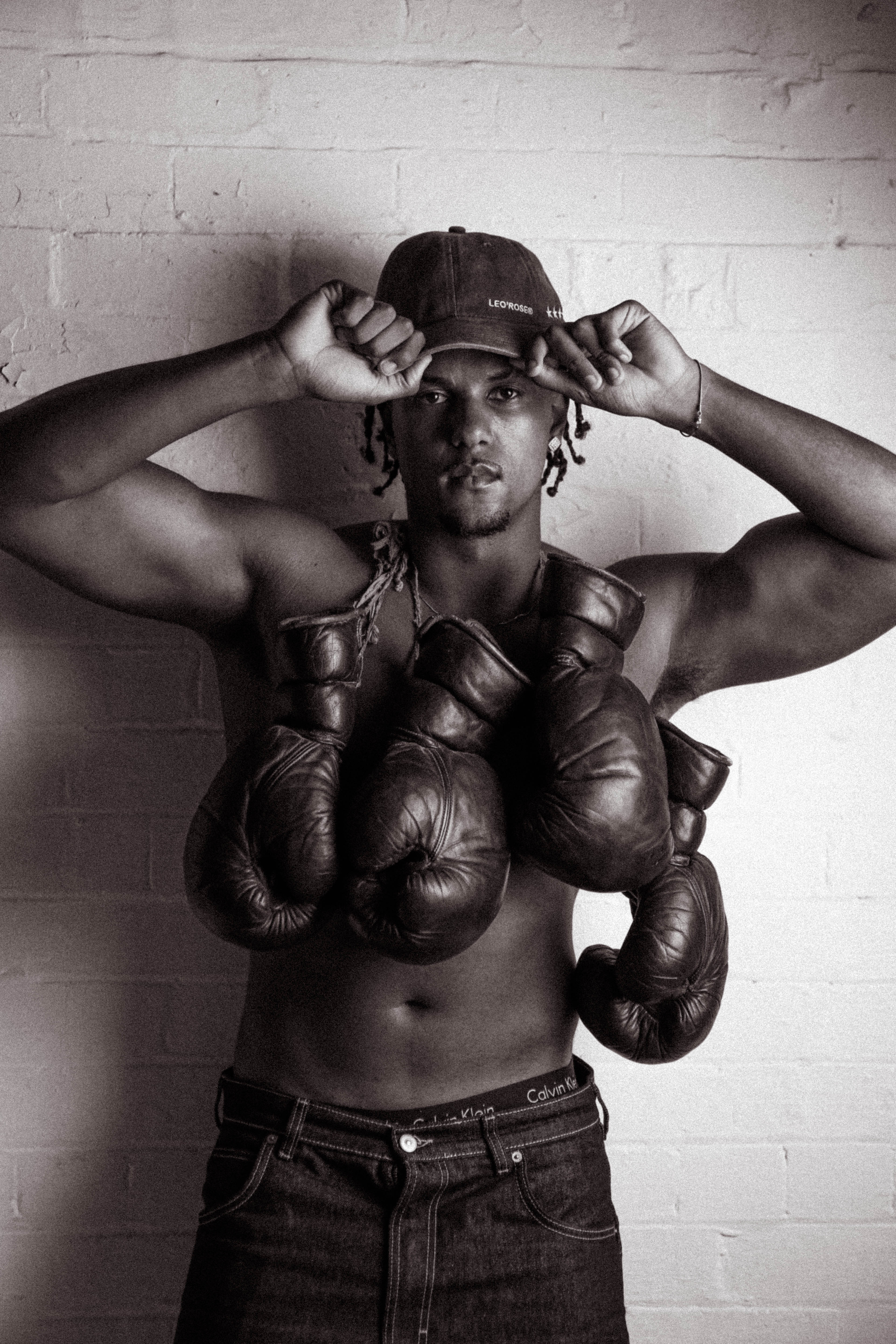 Male looking at camera wearing LEO'ROSE hat with boxing gloves hanging over neck