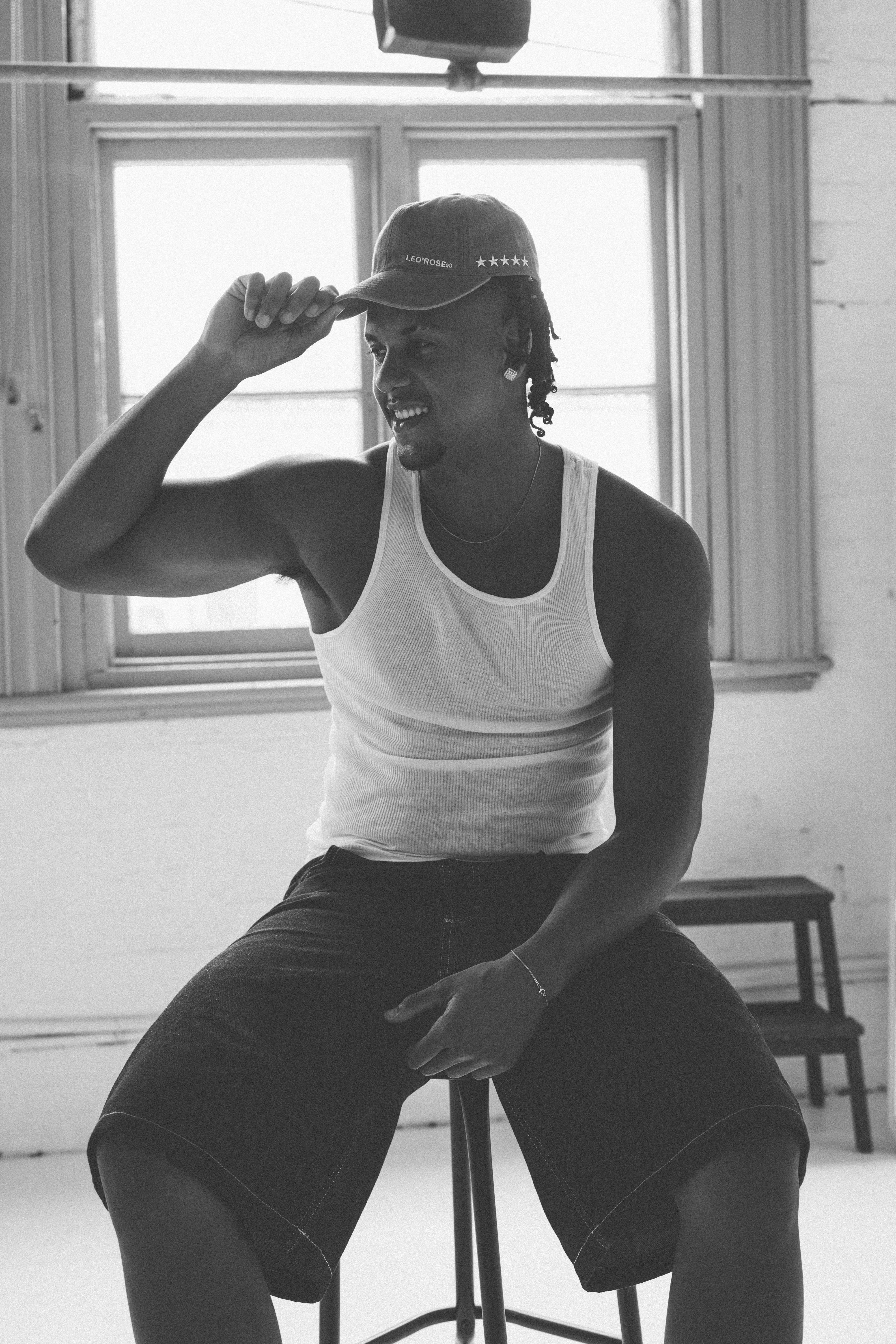 Male sitting on a stool looking away to the left of camera smiling wearing LEO'ROSE hat